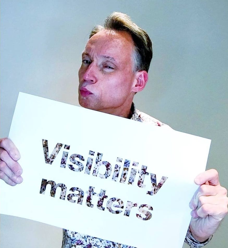 lawrence carter-long holding a sign that says visibility matters